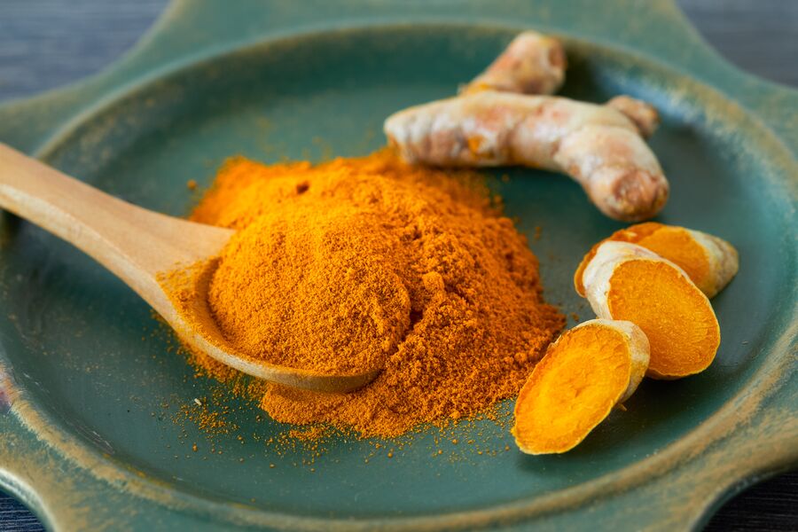 Ground turmeric on a wooden spoon beside fresh turmeric root